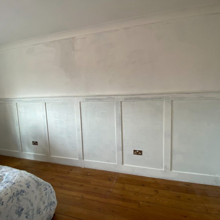 White walls with decorative paneling and wooden floor; empty, bright bedroom.