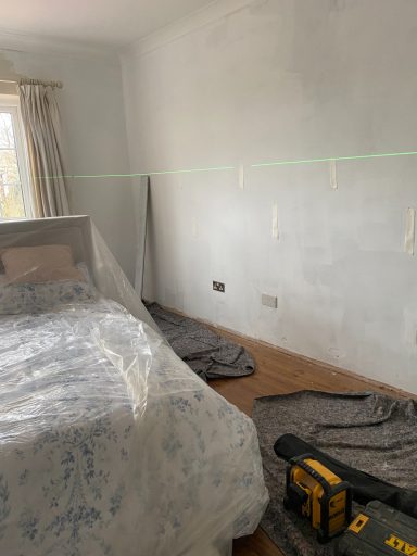 A partially renovated bedroom with a bed, tools, and covered flooring.
