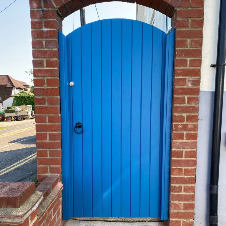 Bright blue wooden door with a curved top, framed by red brick.