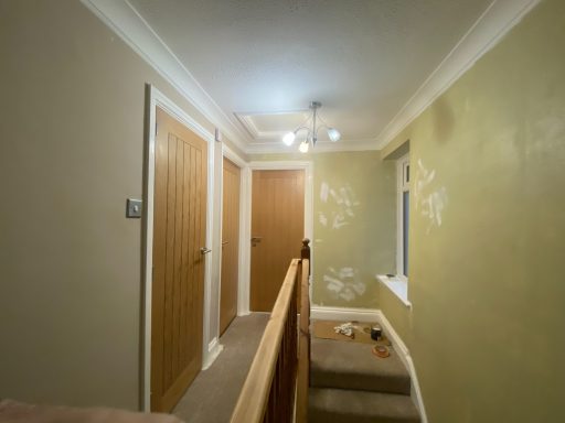 Hallway with wooden doors, beige walls, and unfinished patches of paint.