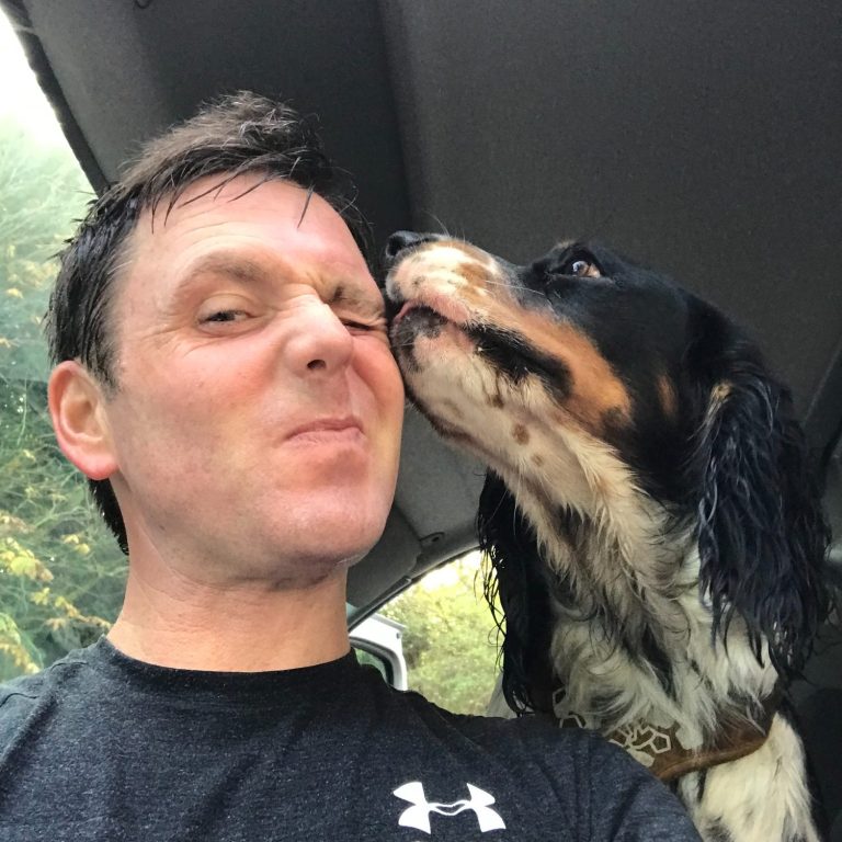 A person smiling while a dog licks their cheek in a car.