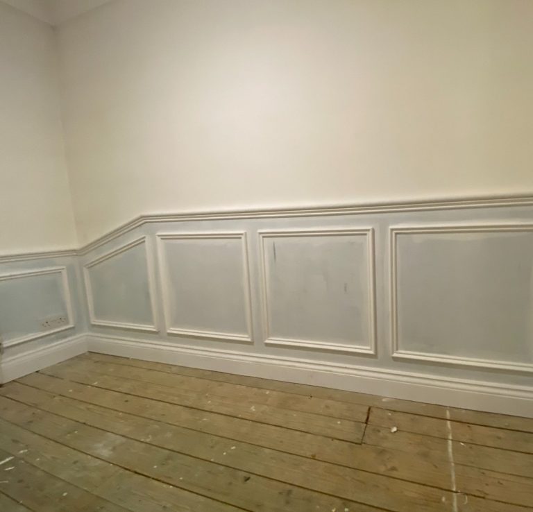 Empty room with light walls and a wooden floor, featuring decorative molding.