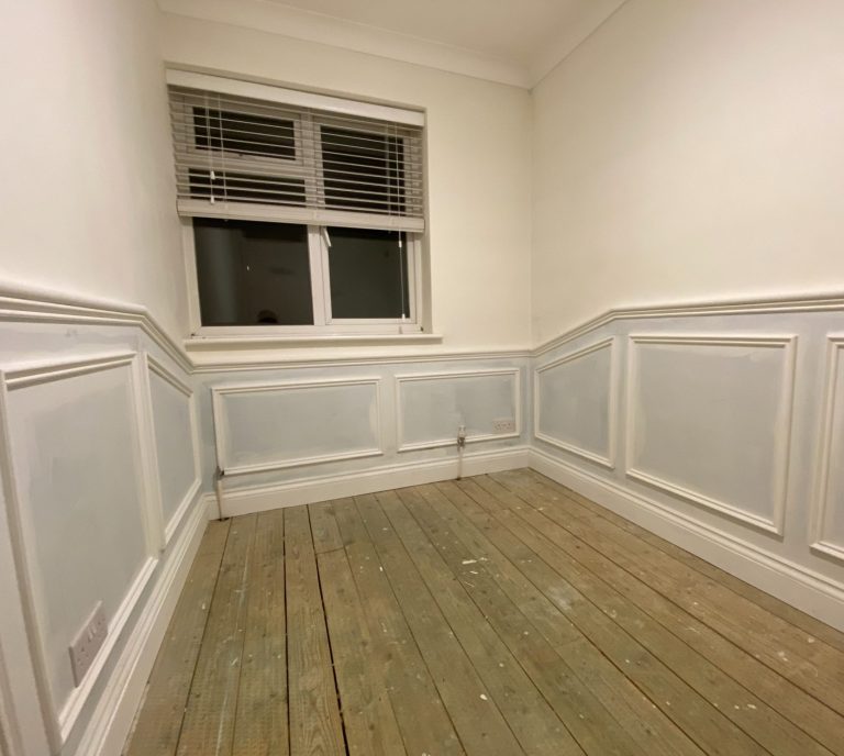 Empty room with wooden floor, pale blue paneling, and a window on the wall.