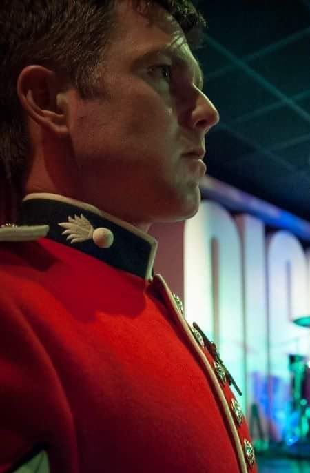 A soldier in a red uniform looks thoughtfully to the side, with a dimly lit background.