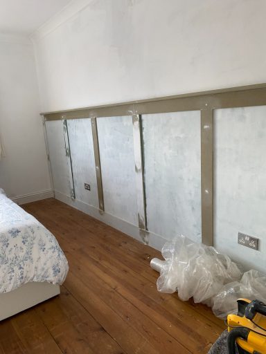 A wooden wall structure with grey panels, next to a bed and scattered building materials.