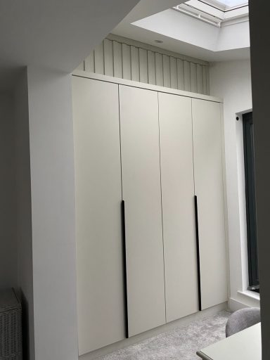 Modern white fitted wardrobes with vertical black handles in a well-lit room.
