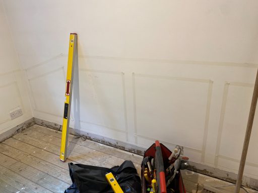 Wall with pencil markings for paneling design beside a level and tools on the floor.