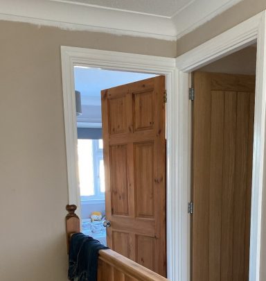 Wooden door partially open, leading to a light-filled room with beige walls.