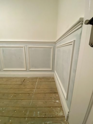 Corner of a room with white walls and wood paneling, featuring a wooden floor.