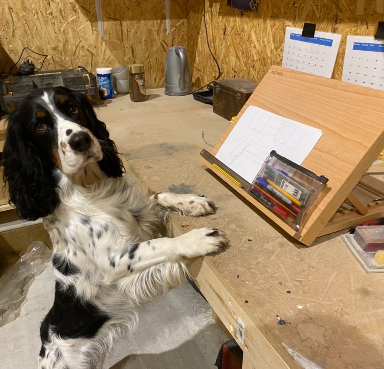 A dog next to a wooden easel on a workbench in a workshop.
