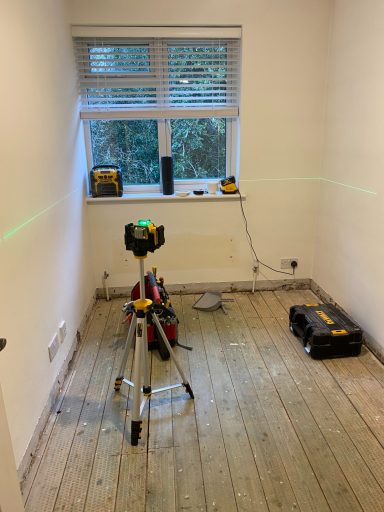A room with a laser level, tools, and wooden floor planks.