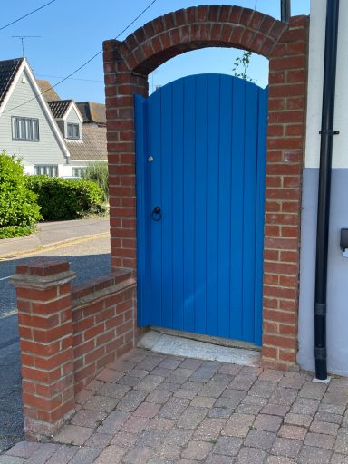 Bright blue door set in a brick archway, with a pathway leading to a house.