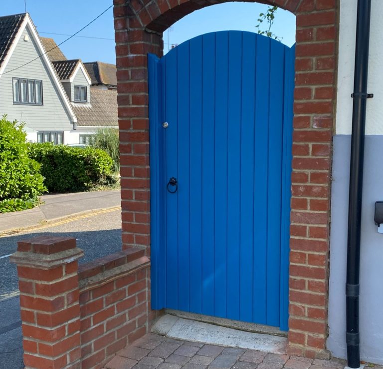 Bright blue gate set in a brick wall, leading to a residential area.