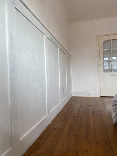 Interior view of a room with white panelled walls and wooden flooring, featuring a door.