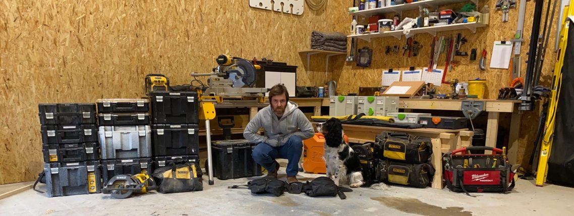 A person sits on the floor in a workshop surrounded by various tools and equipment.