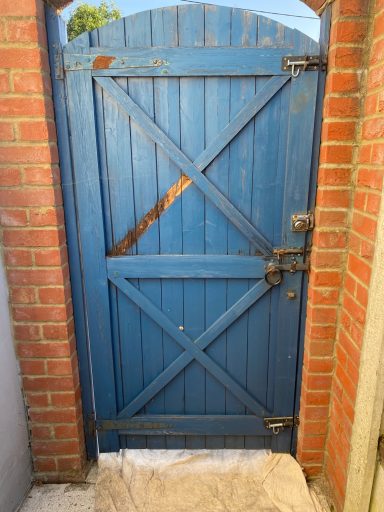 Weathered blue wooden gate set in a red brick wall.
