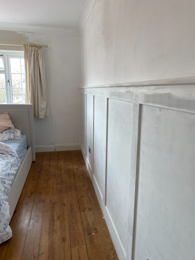 Bedroom corner with a bed, wooden flooring, and a white wall with paneling.