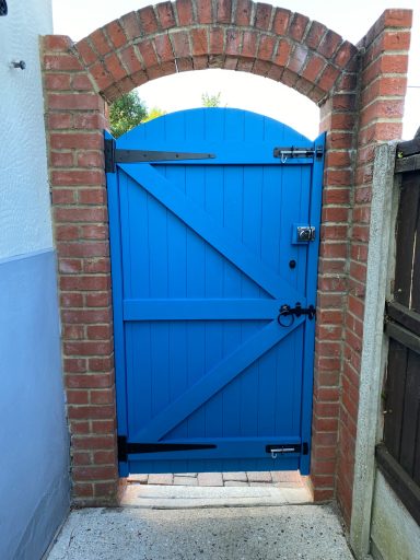A bright blue wooden gate framed by red brick arches and a wooden fence.