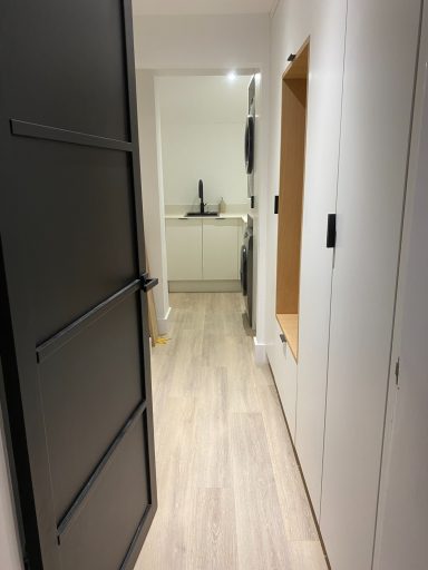 Bright corridor leading to a kitchen, featuring light wooden flooring and modern cabinetry.