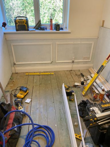 Tools and materials scattered on a wooden floor in a room undergoing renovation.